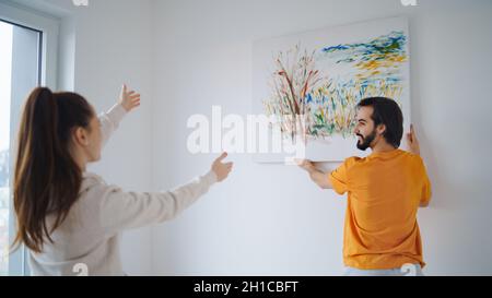 Junges Paar arrangiert neue Wohnung, hängt Malerei, neues Zuhause und Umzugskonzept. Stockfoto