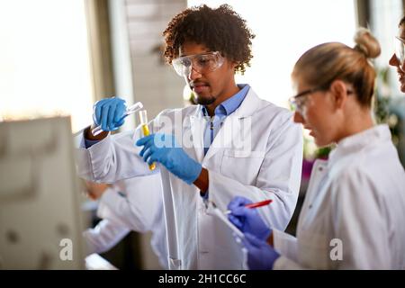 Junge Studenten mischen Chemikalien in einem Reagenzglas und machen sich Notizen über eine chemische Reaktion in einer sterilen Umgebung des Labors. Wissenschaft, Chemie Stockfoto