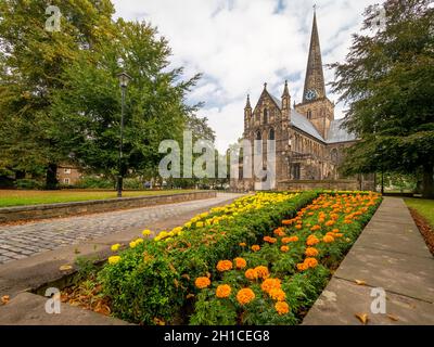Blumenbeet auf dem Kirchhof mit der Kirche des hl. Cuthbert in der Ferne. Darlington. VEREINIGTES KÖNIGREICH. Stockfoto