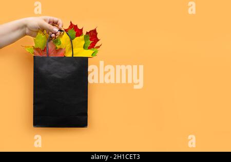 Herbstblätter in einer Tasche auf orangefarbenem Hintergrund. Saisonale Komposition für Layouts, Vorlage mit Ort für Text. Konzept - Herbstangebot, Shopping-Trip Stockfoto