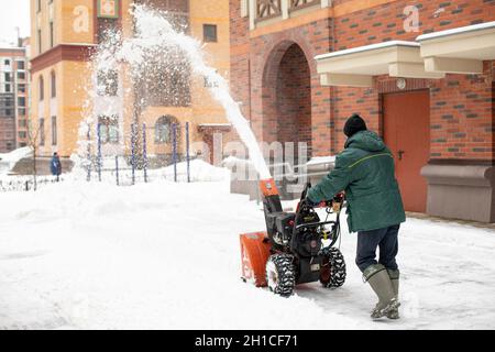 Moskau, Russland - 4. Januar 2021: Ein Mann entfernt Schnee mit einem speziellen Schneefräsen auf Rädern. Aus dem Gerät schießt ein hoher Schneestrahl Stockfoto