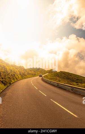 Das Auto fährt auf einer kurvigen Straße mit Sonnenuntergang über der Straße in der Nähe von Lagoa do Fogo mit einer wunderschönen Naturlandschaft. Insel São Miguel auf den Azoren, Portugal. Stockfoto