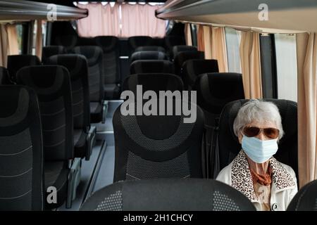 Ältere Beifahrerin in Casualwear und Schutzmaske, die auf dem Sitz im Bus sitzt Stockfoto