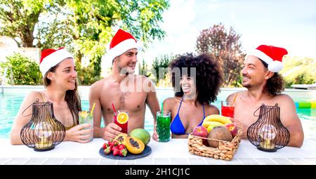frohe weihnachten! Fröhliche, vielfältige Gruppe von Freunden, die Weihnachtsmütze tragen und Cocktail-Drinks auf der Poolparty am Rande der Feier genießen Stockfoto