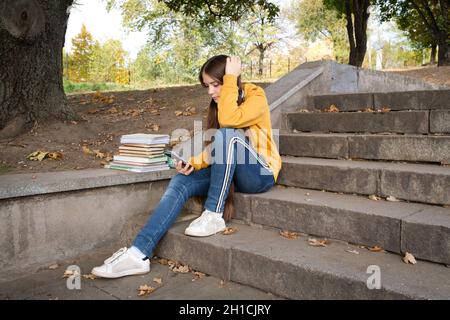 Teenager-Mädchen, das im Herbst auf den Telefonbildschirm schaut, während sie auf der Treppe in der Stadt sitzt Stockfoto