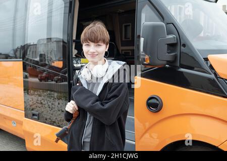 Hübsches Teenager-Mädchen in Casualwear, das Sie anschaut, während Sie vor dem Bus stehen Stockfoto