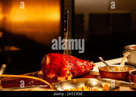 Gebratenes rotes Schweinebein mit Gewürzen, Pfeffer, Fleischgabel in moderner Restaurantküche Stockfoto