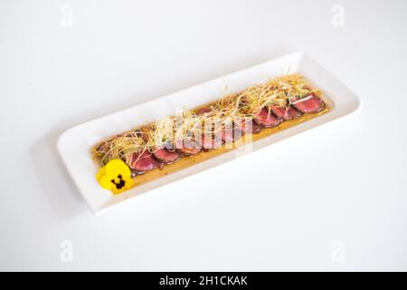 Asiatisches Fleisch in Scheiben geschnitten, mittelgeröstet auf weißem Teller, isoliert auf weißem Hintergrund. Scheiben von mittelgeröstetem Thunfisch. Innen rot, mit Sauce serviert Stockfoto