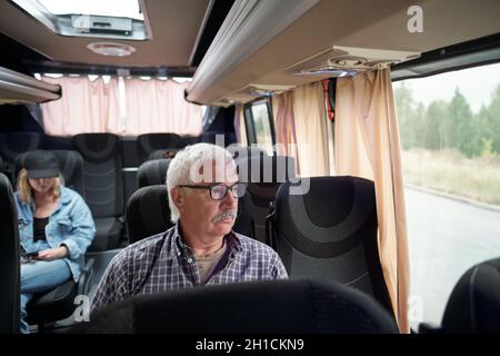 Ernst gealterter Mann in Brillen, der im Bus am Fenster sitzt, während er in eine andere Stadt fährt Stockfoto