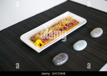 In asiatischem Stil geschnittenes, mittelgeröstetes Fleisch auf weißem Teller auf schwarzer Matte im japanischen Restaurant. Scheiben von mittelgeröstetem Thunfisch mit Sauce. Innen rot. Stockfoto