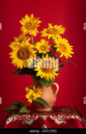 Stillleben. Wunderschöne Sonnenblumen in Keramikkrug auf rotem Hintergrund Stockfoto