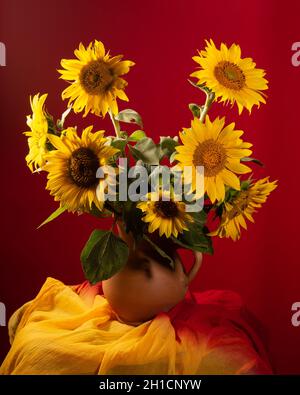 Stillleben. Wunderschöne Sonnenblumen in Keramikkrug auf rotem Hintergrund Stockfoto