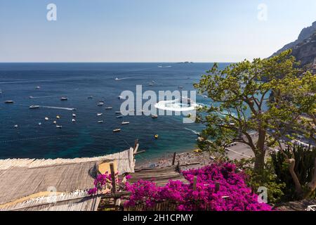 Positano, Italien, 12. Juni 2017: Positano durch rosafarbene Bougainvillea und Boote im Hintergrund eingerahmt. Bunte Positano, die Perle der Amalfiküste, Stockfoto