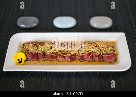 In asiatischem Stil geschnittenes, mittelgeröstetes Fleisch auf weißem Teller auf schwarzer Matte im japanischen Restaurant. Scheiben von mittelgeröstetem Thunfisch mit Sauce. Innen rot. Stockfoto