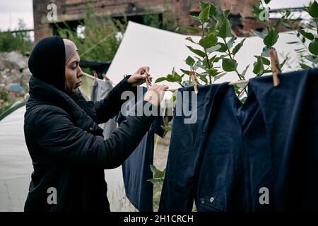 Junge Migrantinnen hängen saubere Kleidung an einem Seil gegen die Besiedlung im Lager Stockfoto