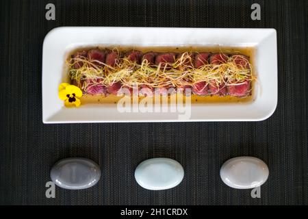 In asiatischem Stil geschnittenes, mittelgeröstetes Fleisch auf weißem Teller auf schwarzer Matte im japanischen Restaurant. Scheiben von mittelgeröstetem Thunfisch mit Sauce. Innen rot. Stockfoto