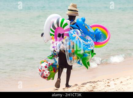 Santa Margherita di Pula, Italien - 05. Juli 2016: Ehrliches Bild von schwarzen Arbeitslosen, die am heißen Sommertag am Strand spazieren gehen und Spielzeug verkaufen und sein Stockfoto