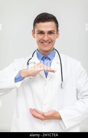 Ein lächelnder Arzt steht nach vorne und hat seine Hände angehoben, um für ein neues Produkt zu werben. Stockfoto