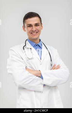 Der lächelnde Arzt steht mit gefalteten Händen in einem sanften Lächeln nach vorne. Stockfoto