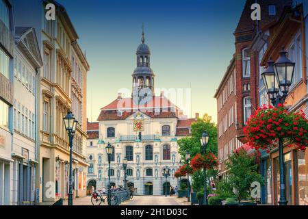 LÜNEBURG, NIEDERSACHSEN, DEUTSCHLAND - 27. JULI 2018: Alte Straßenlaterne mit Blumenbeet. Historisches Rathaus im Hintergrund in Lüneburg Deutsch Stockfoto