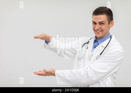 Ein lächelnder Arzt steht nach vorne und hat seine Hände angehoben, um für ein neues Produkt zu werben. Stockfoto