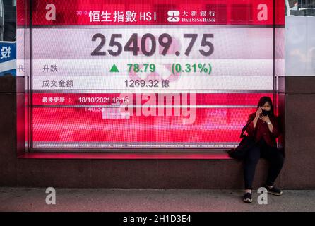 Hongkong, China. Oktober 2021. Eine Frau sitzt neben einer Börsendisplagetafel, auf der die Informationen zum Hang Seng Index angezeigt werden.Kredit: SOPA Images Limited/Alamy Live News Stockfoto