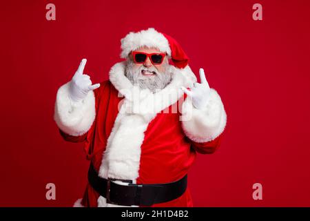 Portrait von attraktiven verrückten Santa zeigt Horn Symbol mit Spaß Neujahr Gelegenheit isoliert über hellen roten Hintergrund Stockfoto