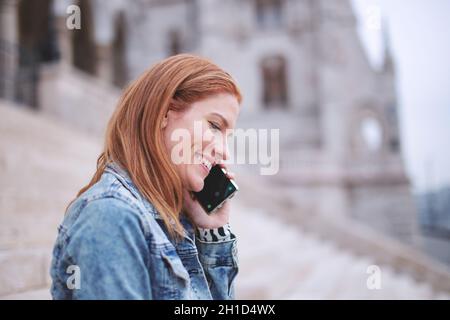 Glückliche junge kaukasische positive Rotschopf Frau in der Stadt, Budapest, Ungarn anrufen Stockfoto