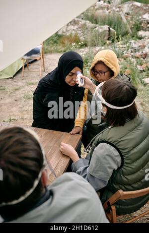 Ehrenamtlicher Arzt zur Messung der Körpertemperatur junger Frauen in Hijab auf dem Territorium des Flüchtlingslagers Stockfoto