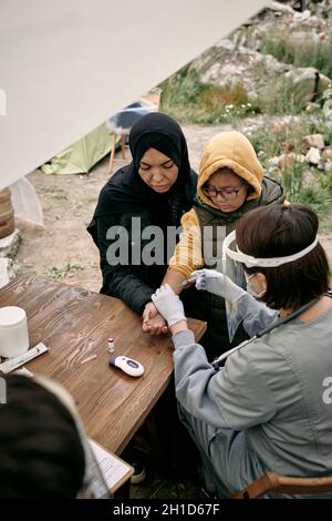 Weibliche Freiwillige oder Ärztin, die das kleine Mädchen und ihre Mutter im Flüchtlingslager impft Stockfoto