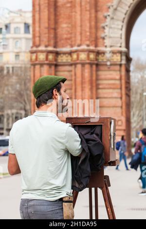 BARCELONA - MÄRZ 2018: Junger männlicher Fotograf, der mit einer alten Holzkamera am Triumphbogen in Barcelona fotografiert Stockfoto