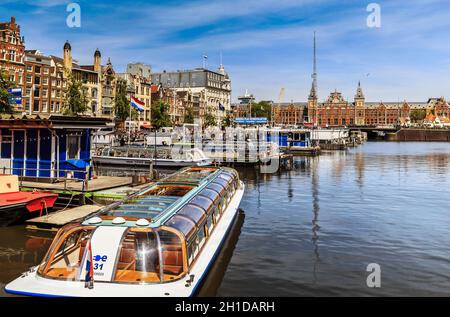 Amsterdam, Niederlande - 23. Mai 2019: Kanalblick mit Booten von der Straße Damrak. Die Centraal Station ist im Hintergrund. Stockfoto