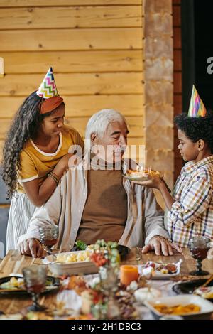 Großvater bläst Kerzen auf den Kuchen, während Enkel ihm zum Geburtstag gratulierten Stockfoto