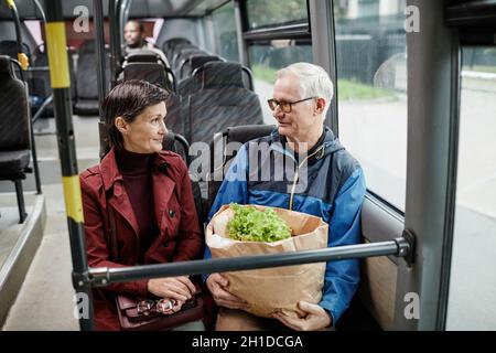 Porträt eines erwachsenen Paares, das im Bus plaudert, während er mit öffentlichen Verkehrsmitteln in der Stadt unterwegs ist, Kopierraum Stockfoto