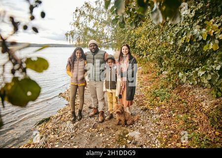 Porträt einer glücklichen vierköpfigen Familie, die die Kamera umarmt und lächelt, während sie gemeinsam im Herbstwald spazieren geht Stockfoto