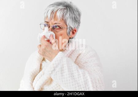 Coronavirus-Pandemie. Gesundheits-, Grippe-, Hygiene- und Personkonzept. Kranke Seniorin mit Papierwischtuch, die zu Hause die Nase weht. Stockfoto