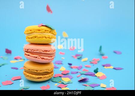 Bunte Makronen auf modischem pastellblauem Papier mit Konfetti. Schmackhafte Rosa-, Gelb- und Braunmakronen. Stockfoto