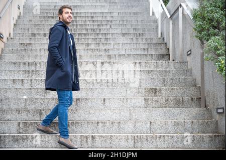 Horizontale Porträt der jungen attraktiven Mann stehend auf Schritte zurück zu schauen. Die modernen und stilvollen Kerl hält Laptop Hände. Stockfoto