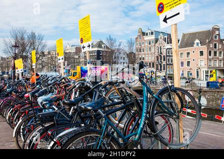 AMSTERDAM, NIEDERLANDE - MÄRZ, 2018: Ein Haufen Fahrräder, die neben dem Kanal im Old Central District in Amsterdam geparkt sind Stockfoto