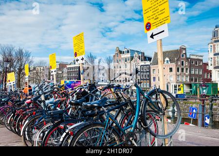 AMSTERDAM, NIEDERLANDE - MÄRZ, 2018: Ein Haufen Fahrräder, die neben dem Kanal im Old Central District in Amsterdam geparkt sind Stockfoto