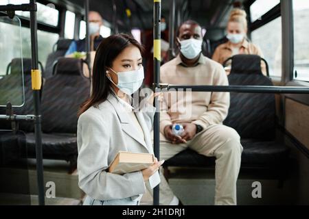 Seitenansicht Porträt einer jungen asiatischen Frau mit Maske im Bus, während sie mit öffentlichen Verkehrsmitteln in der Stadt unterwegs ist, Kopierraum Stockfoto