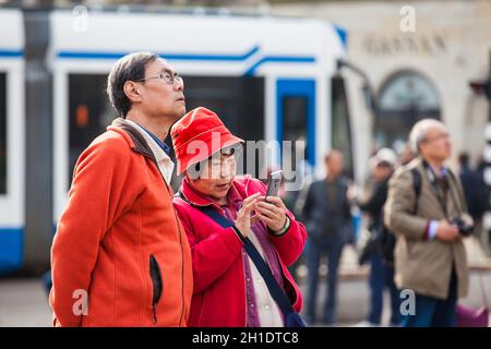 AMSTERDAM, NIEDERLANDE - MÄRZ 2018: asiatische Touristen mit ihren Handys Fotos am Dam in Amsterdam zu nehmen Stockfoto
