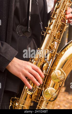 Eine Frau spielt Saxophon in einem Herbstpark. Nahaufnahme des goldenen Saxophons Stockfoto