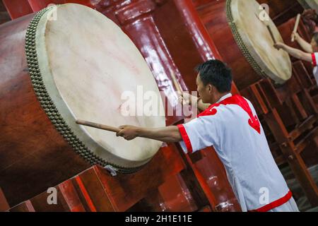 Ein junger Mann in weißem Anzug spielt eine alte chinesische Trommel. Stockfoto