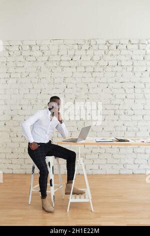 Lächelnder afrikanischer Mann, der zu Hause am Tisch sitzt. Konzept von jungen Menschen mit Laptop. Stockfoto