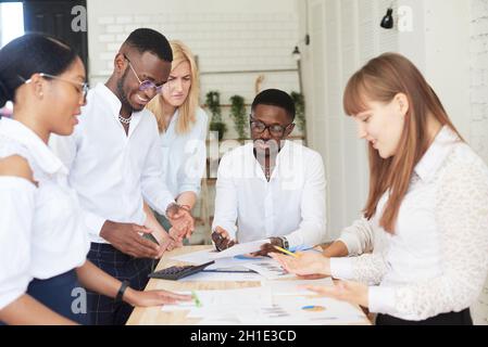 Ein Team aus multiethnischen Personen diskutiert im Büro über Geschäfte. Die Mitarbeiter des Unternehmens kommunizieren, betrachten die Zeitpläne und diskutieren Stockfoto