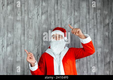 Kaukasischer junger Mann, der als Weihnachtsmann gekleidet war und mit beiden Händen nach links zeigte. Platz darüber kopieren Stockfoto