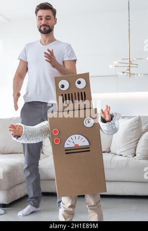 Fröhliche Familie Vater und Sohn spielen tanzen wie Roboter zu Hause, Kinder tragen handgemachte Moving Box Kostüm aus Pappe Stockfoto