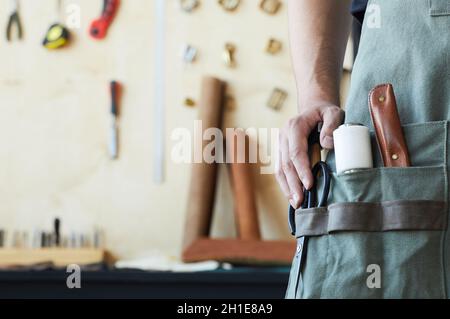 Nahaufnahme verschiedener Ledermacherwerkzeuge in der Schürzentasche des männlichen Gerbers, Kopierraum Stockfoto