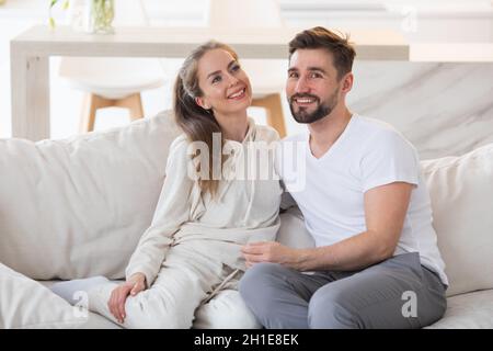 Ein junges, schönes Paar, das zu Hause lächelt und auf einem Sofa sitzt Stockfoto